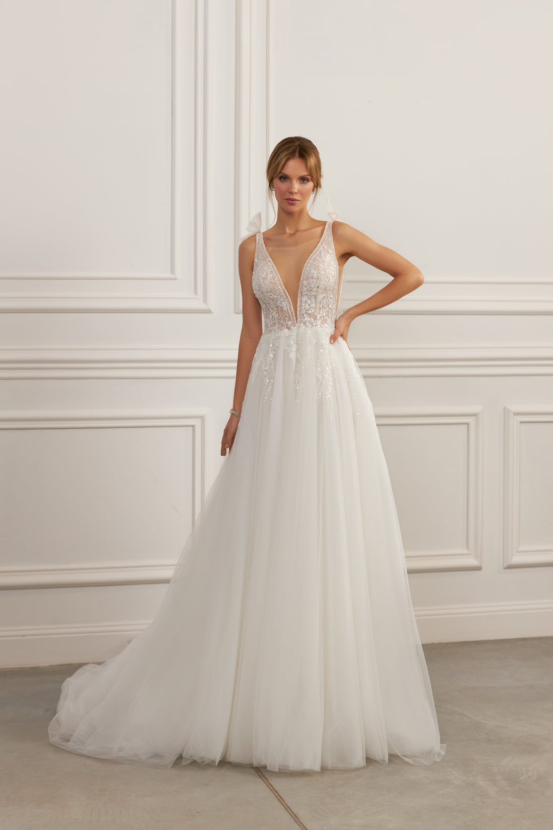 Sleeveless A-line gown - Plunging neckline bridal dress - Lace and beadwork dress - Bow-tied shoulder straps - Fitted bodice with lace - Voluminous tulle skirt - Elegant wedding dress - Formal bridal gown - Modern sophisticated dress - Timeless beauty gown